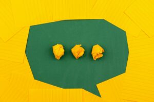 three crumpled yellow papers on green surface surrounded by yellow lined papers communication